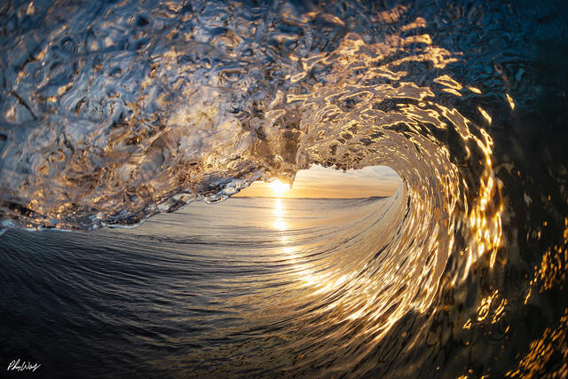 Golden sunrise light shining through the inside of a hollow ocean wave in Oxnard, California.