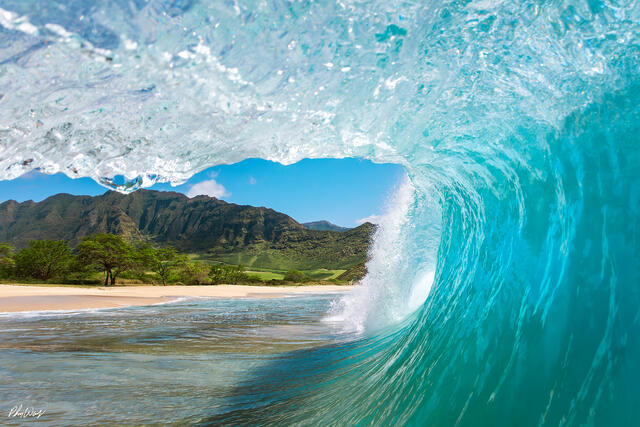 Turquoise ocean wave curling near a tropical beach with mountains in Oahu Hawaii.