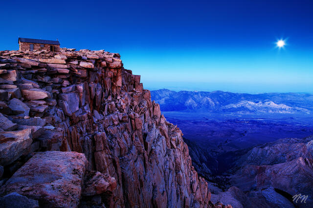Mount Whitney summit shelter on a rocky granite cliff at moonrise in Sequoia National Park, California, overlooking the Sierra Nevada mountains and valley below