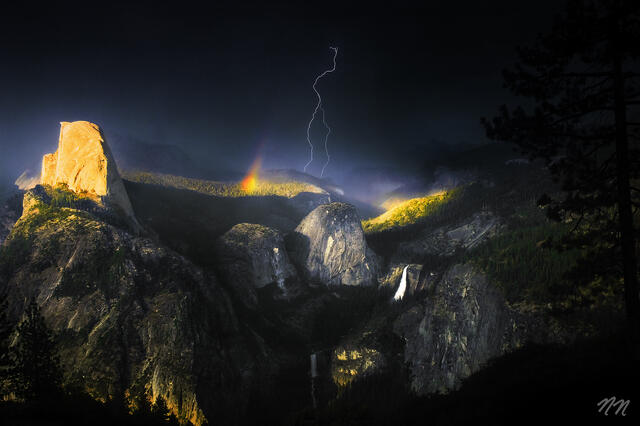 Lightning strike behind a rainbow over Half Dome, Vernal Fall, and Nevada Fall during a storm in Yosemite National Park, California.
